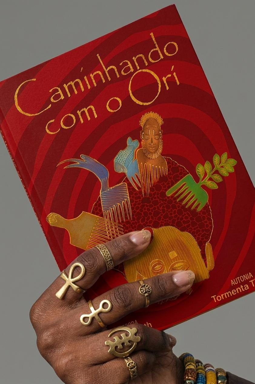 Mão com anéis de Ankh e Adinkra segurando a capa vermelha de Caminhando com o Orí